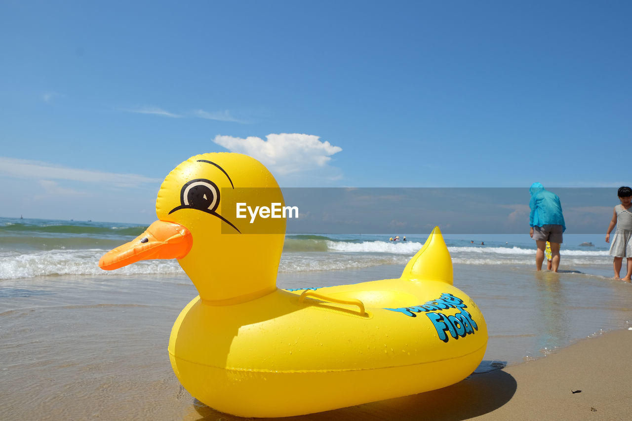 CLOSE-UP OF YELLOW TOY BY SEA AGAINST SKY