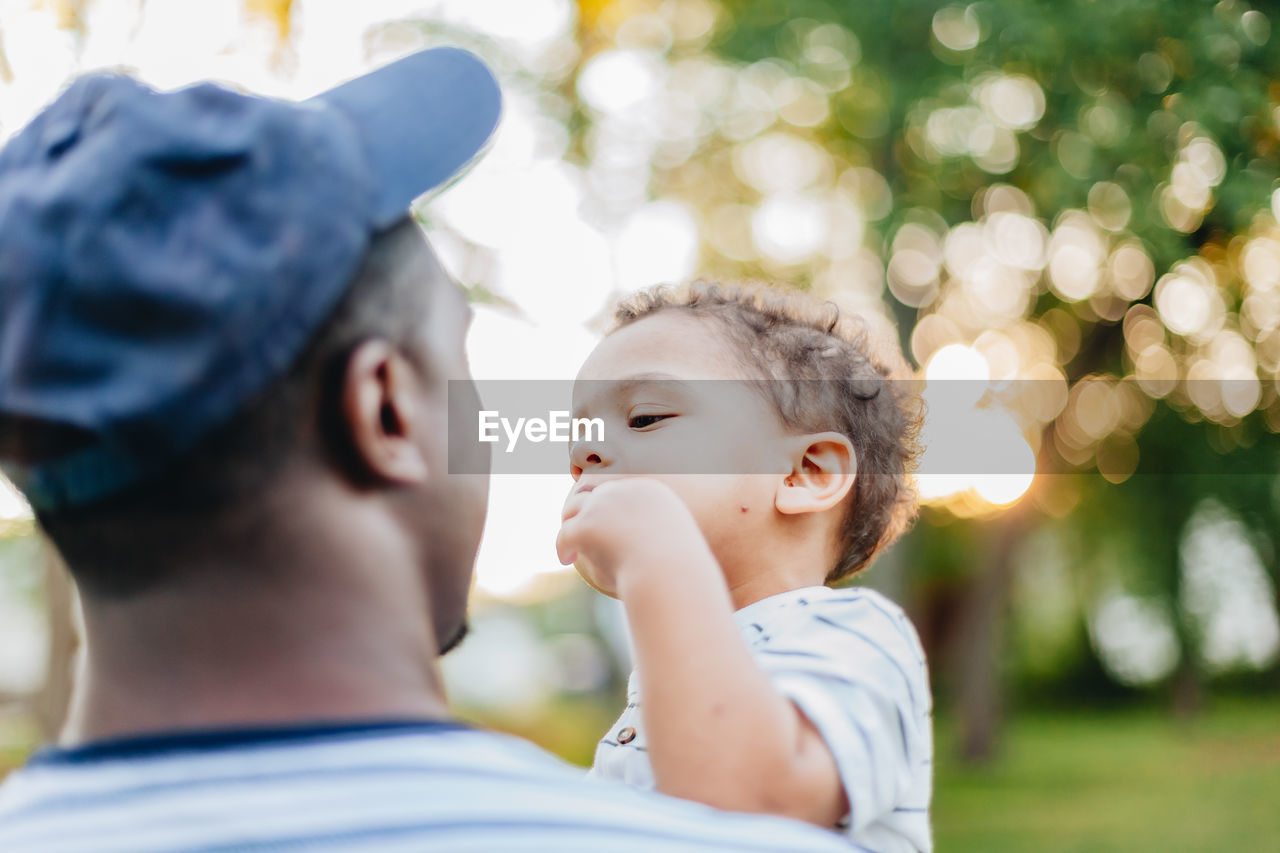 Young millennial african american father and mixed race diverse son bonding at park summer day