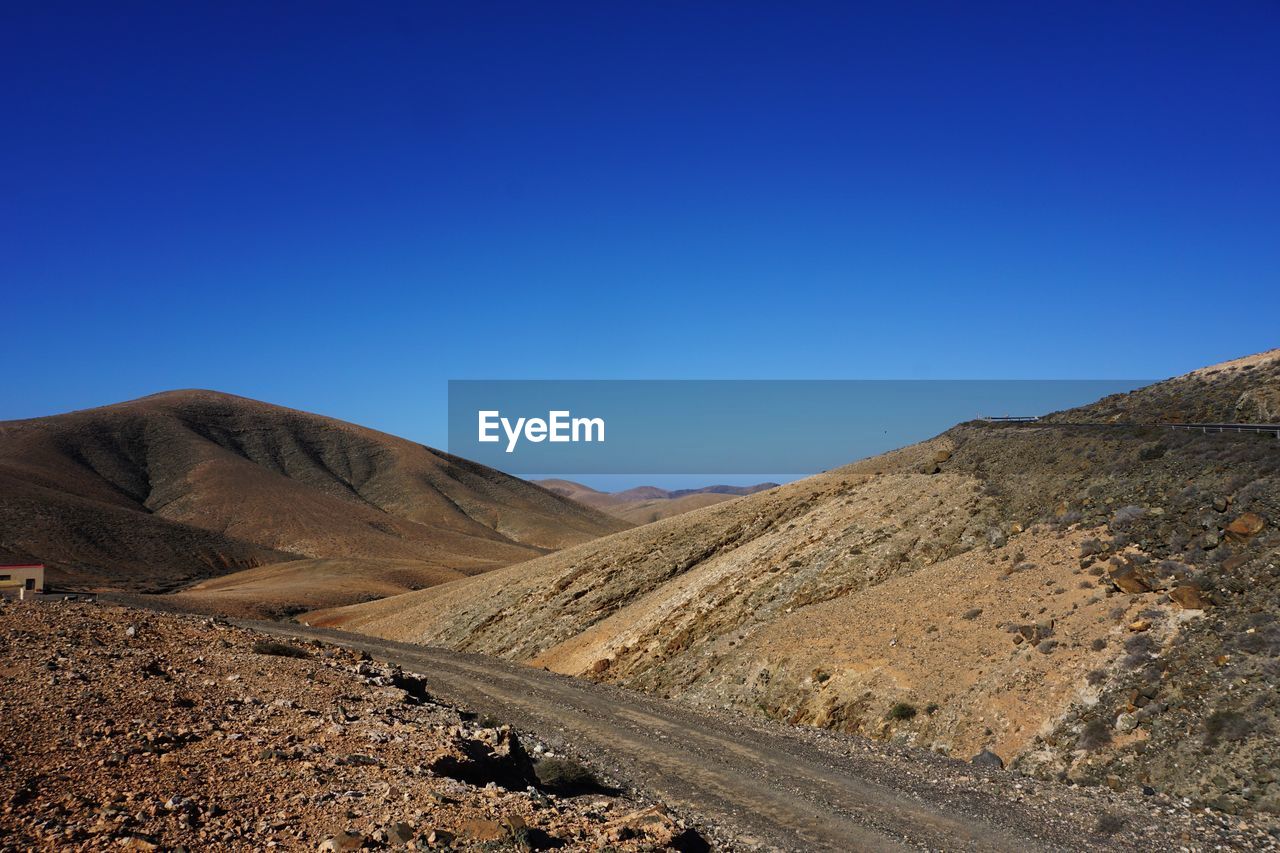 Scenic view of arid landscape against clear blue sky