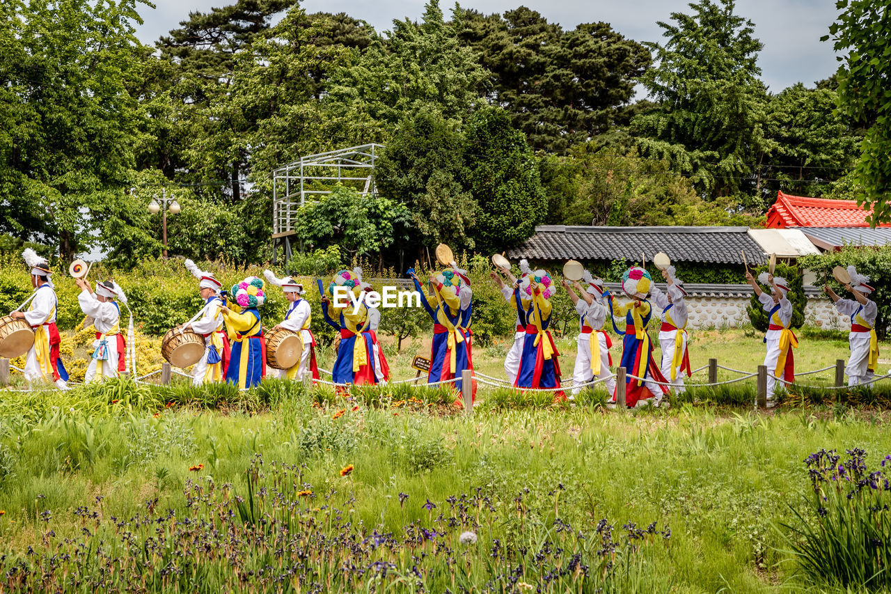 GROUP OF PEOPLE STANDING ON FIELD BY TREE