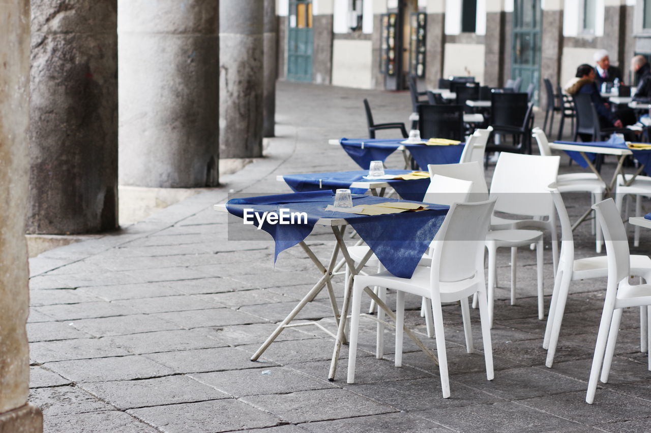 Empty chairs and tables arranged at sidewalk cafe