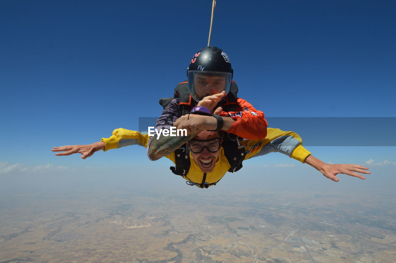 Portrait of men skydiving against blue sky