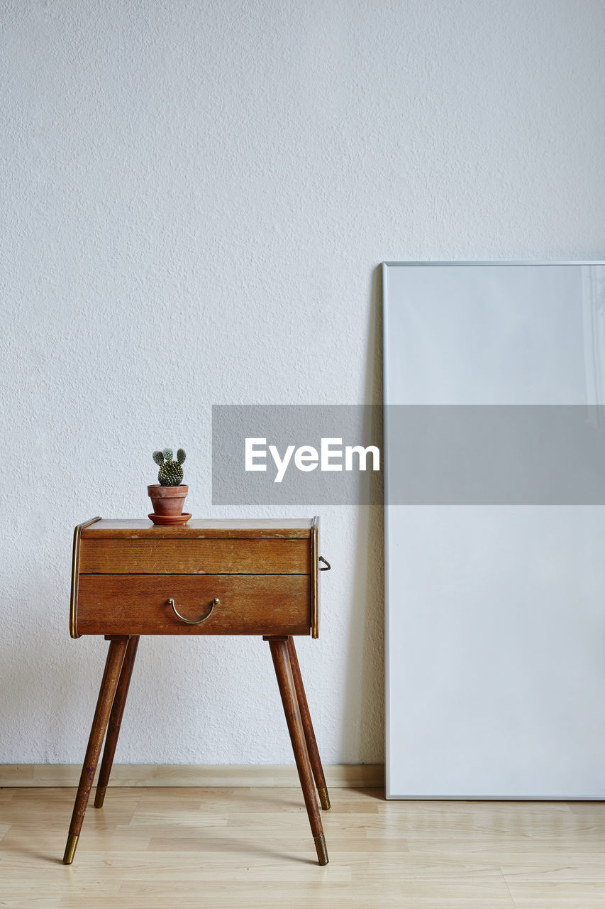 Potted plant on drawer with picture frame by wall