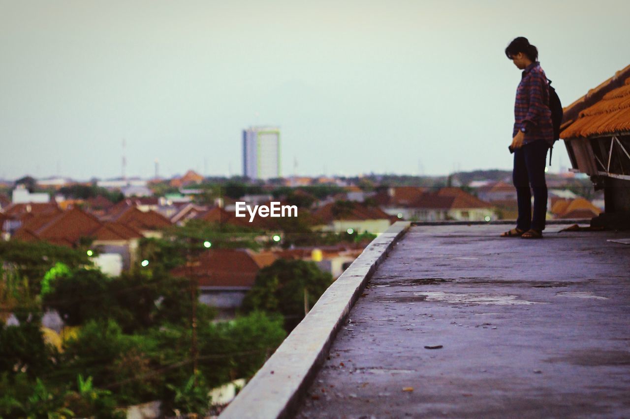 Side view of man standing on terrace in city against clear sky