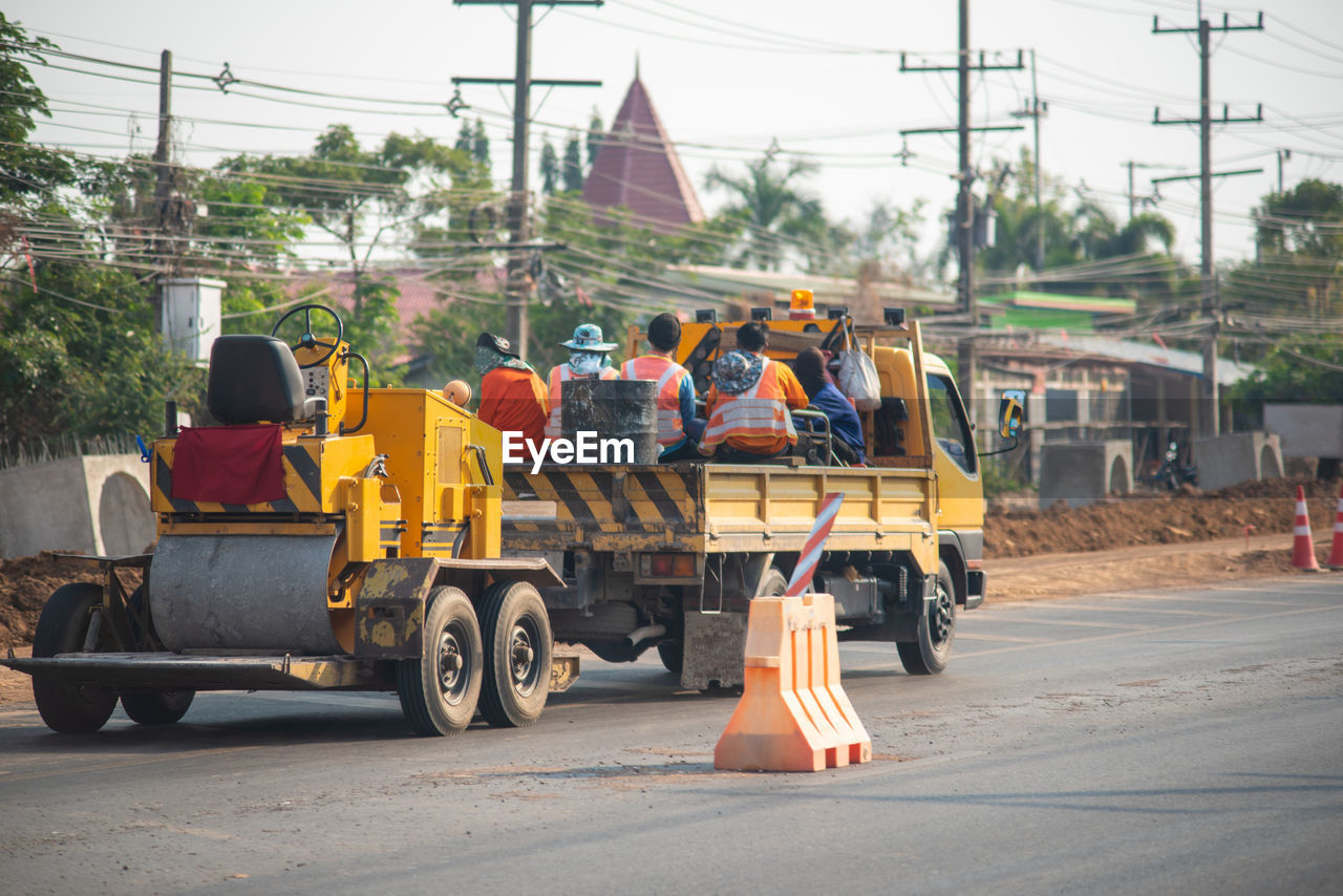 PEOPLE WORKING ON ROAD IN CITY AGAINST SKY