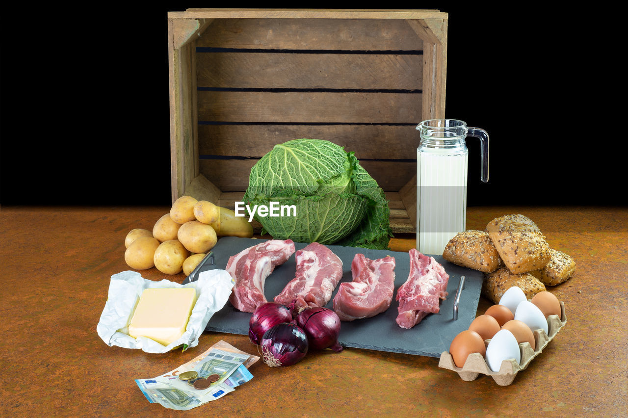 Food for basic needs. in the background is a wooden fruit box. in the foreground are euro banknotes.