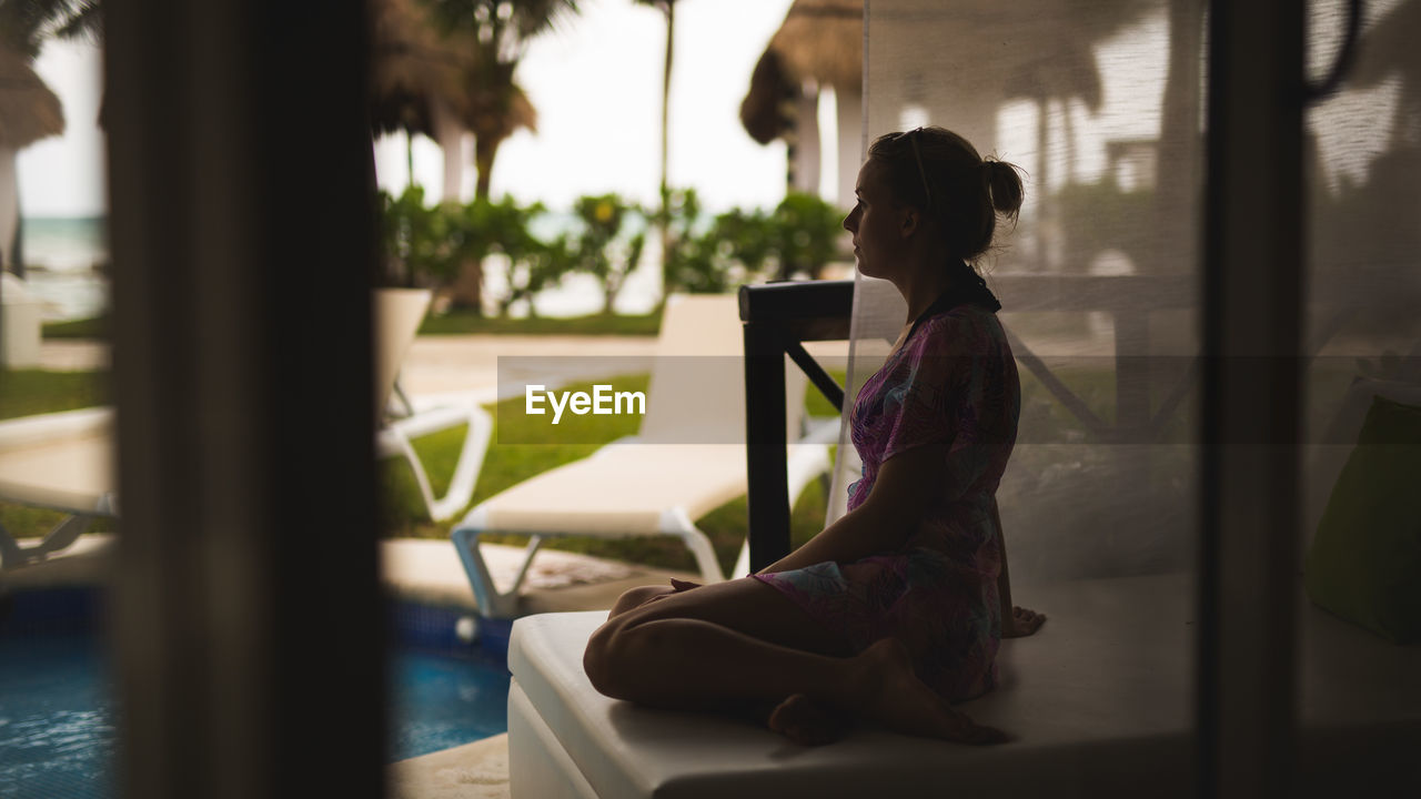 Side view of woman relaxing on seat by swimming pool