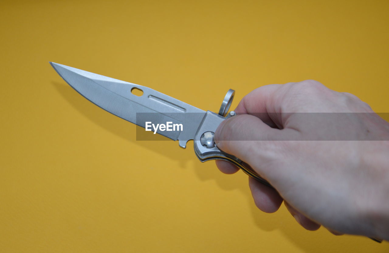 knife, hand, melee weapon, weapon, utility knife, hunting knife, kitchen knife, studio shot, yellow, one person, indoors, colored background, tool, blade, bowie knife, adult, sharp, close-up, holding, warning sign, cold weapon