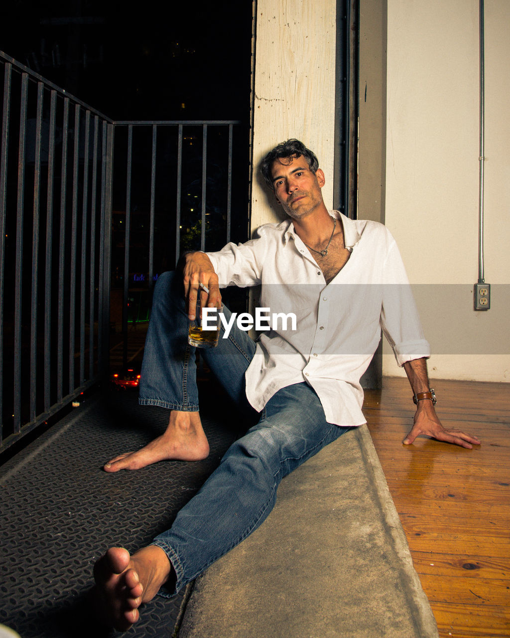 Portrait of man with whiskey and cigarette sitting in balcony at night