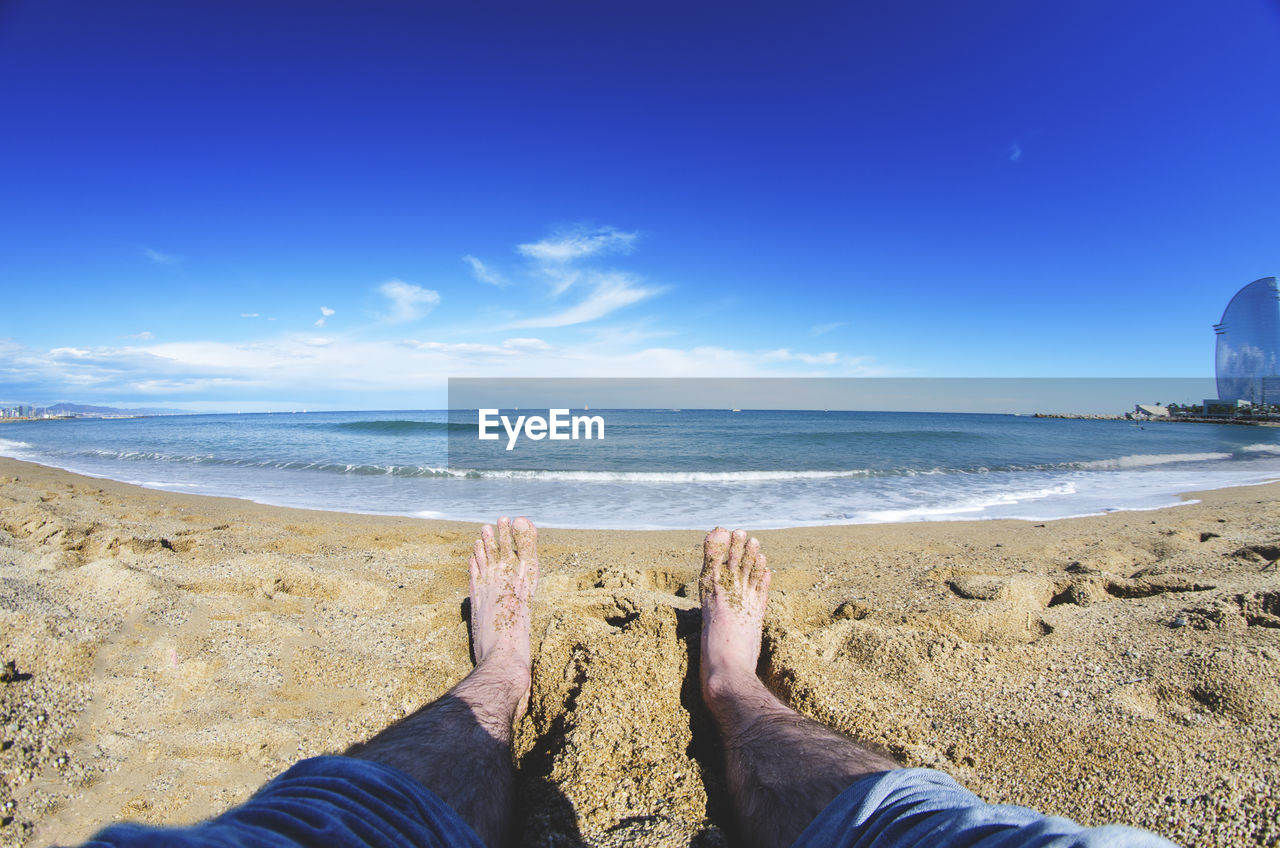 Low section of man sitting at beach against sky