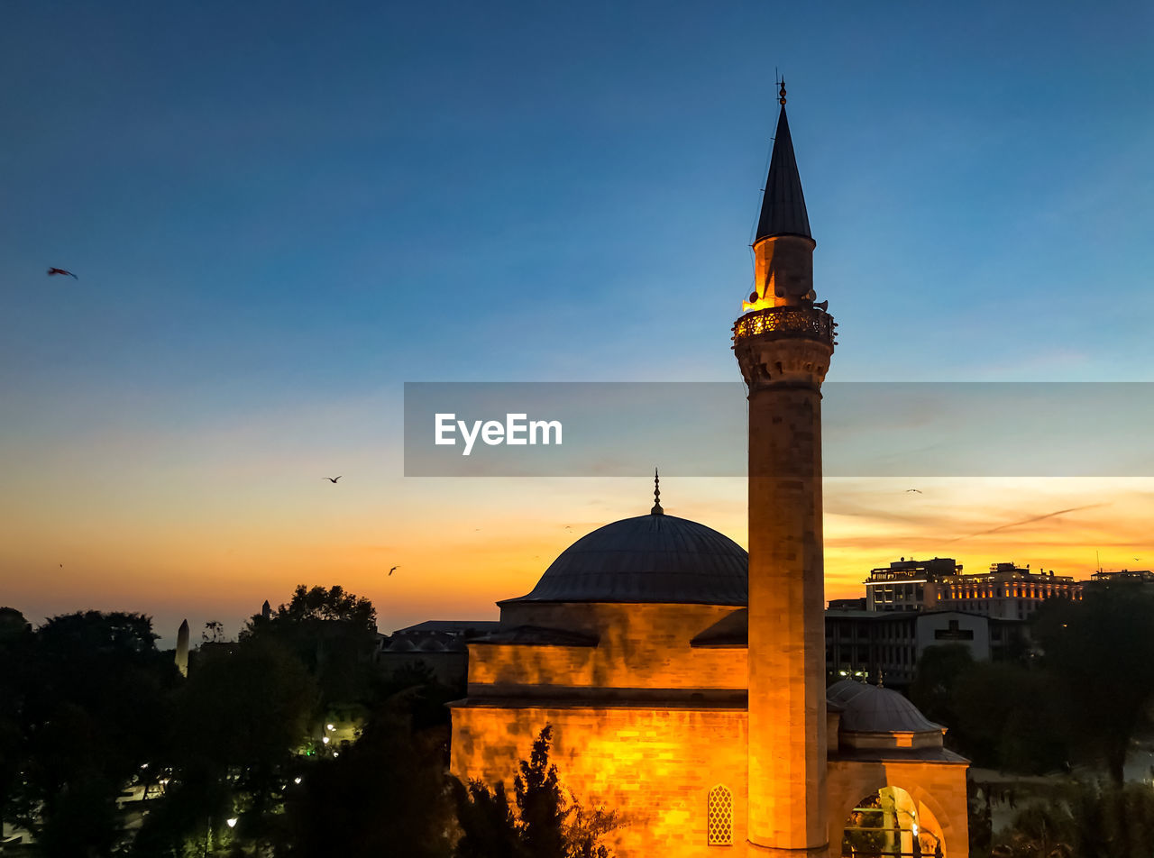 Tower amidst buildings against sky during sunset