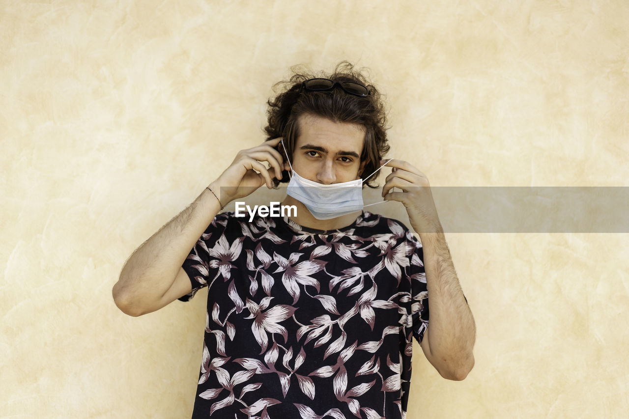 Portrait of young man wearing mask standing against wall