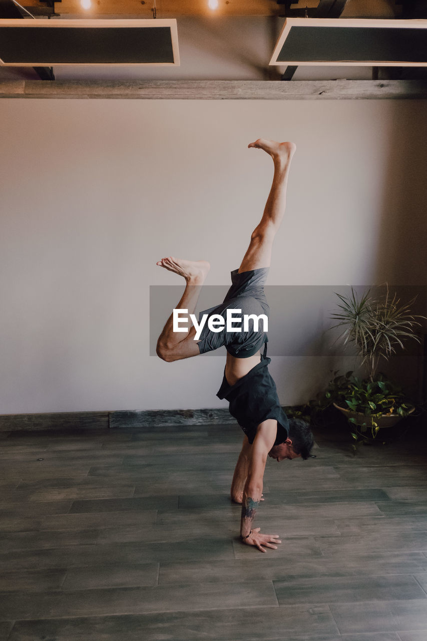 Back view of faceless barefooted man in sportswear standing upside down in downward facing dog pose while training in contemporary gym