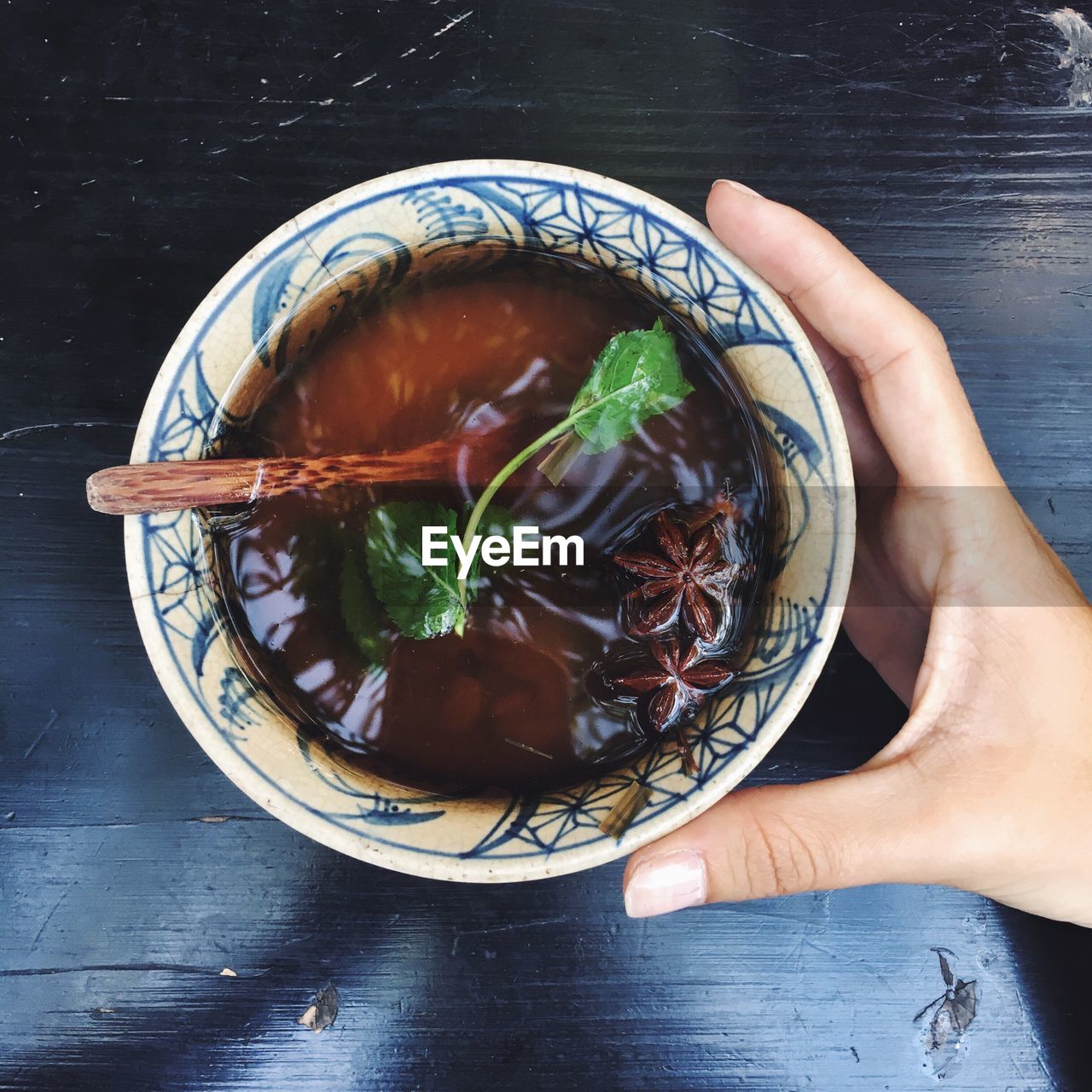 Cropped hand of woman holding herbal tea bowl on table