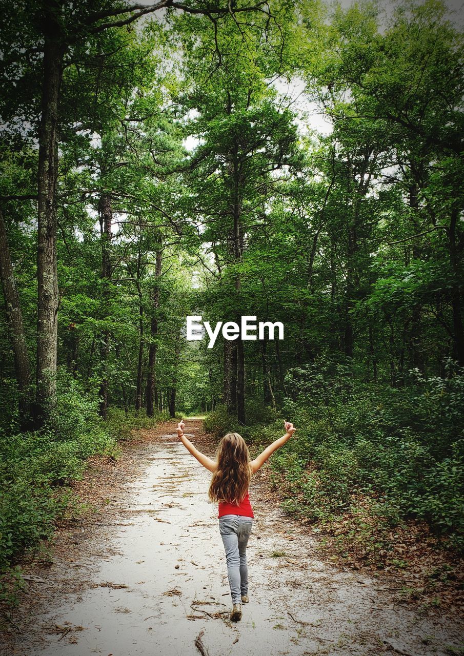 Rear view of girl with arms raised walking on footpath in forest