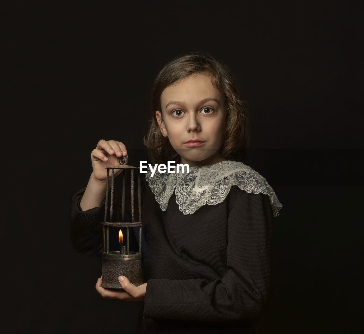 Portrait of a kid holding oil lamp against black background