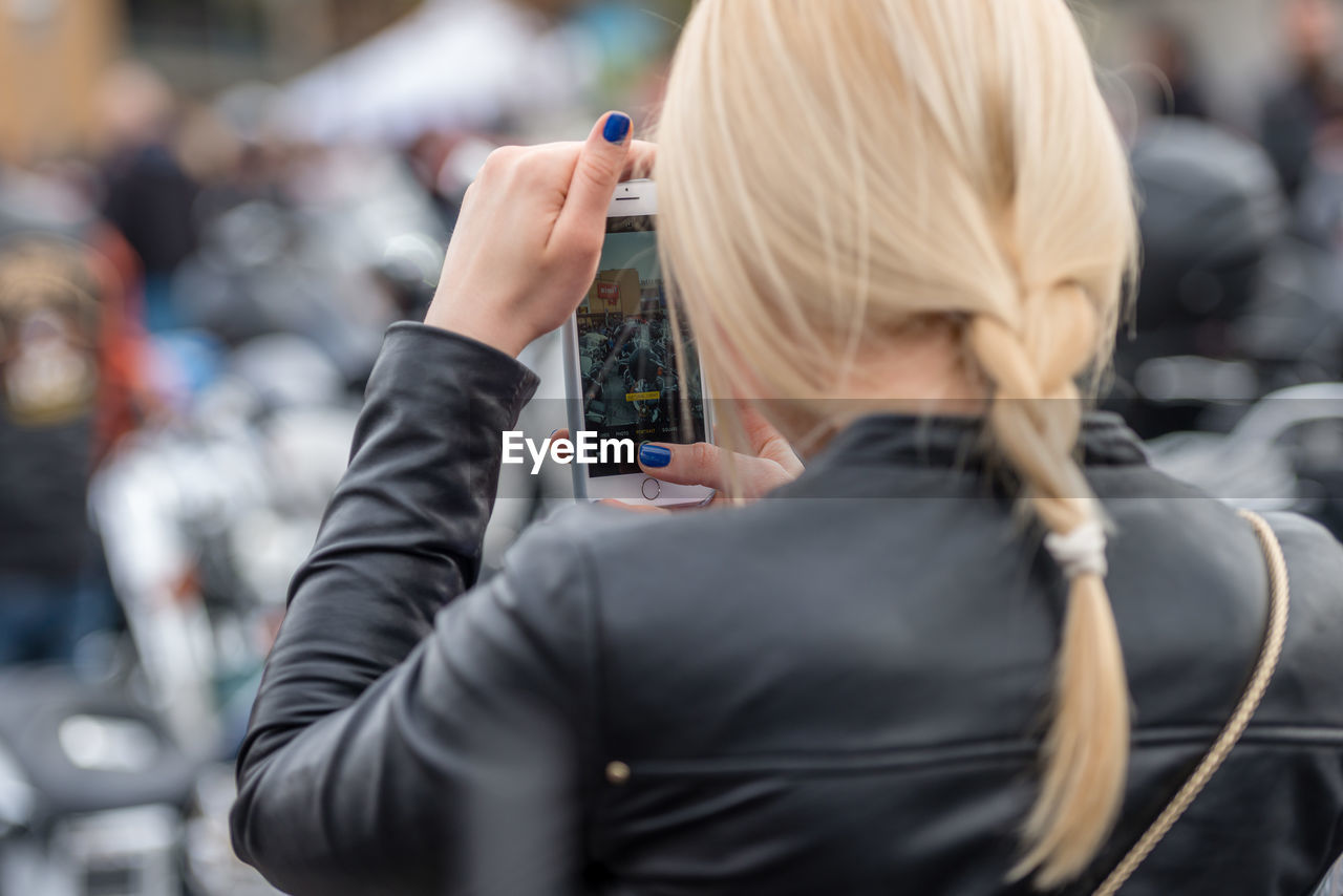 Rear view of woman photographing through mobile phone