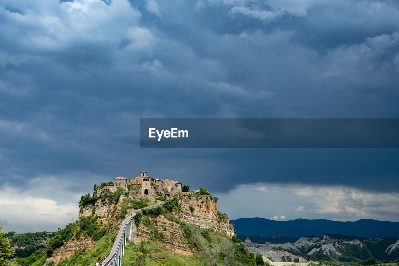 cloud, sky, mountain, environment, nature, landscape, scenics - nature, architecture, travel destinations, beauty in nature, mountain range, land, travel, sea, built structure, dramatic sky, horizon, tourism, storm, building, outdoors, no people, plant, overcast, rock, building exterior, cloudscape, tree, storm cloud, history, blue, tranquility, non-urban scene, the past, coast, day, water, tranquil scene, cliff, plateau, trip, forest, holiday