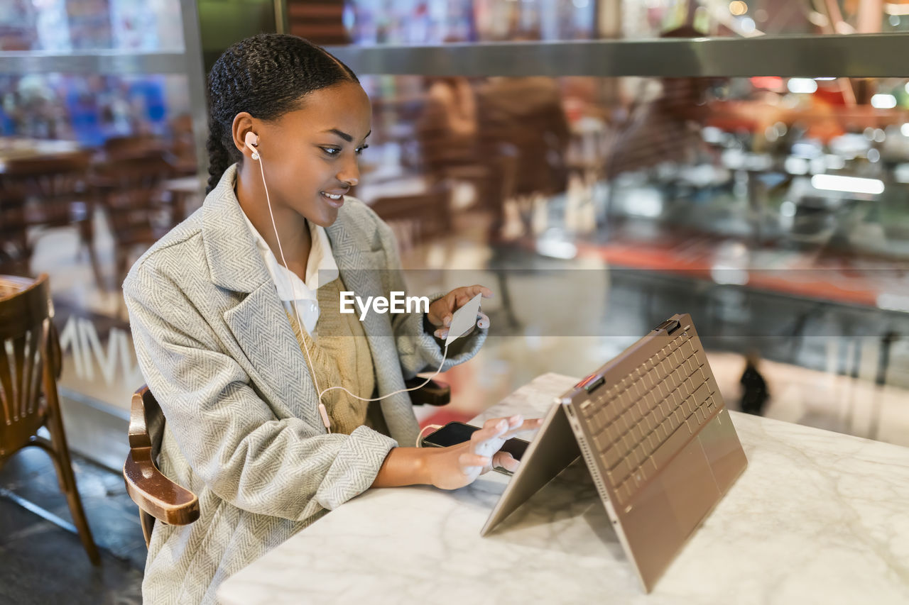 Girl making online payment through credit card on touch screen laptop at cafe