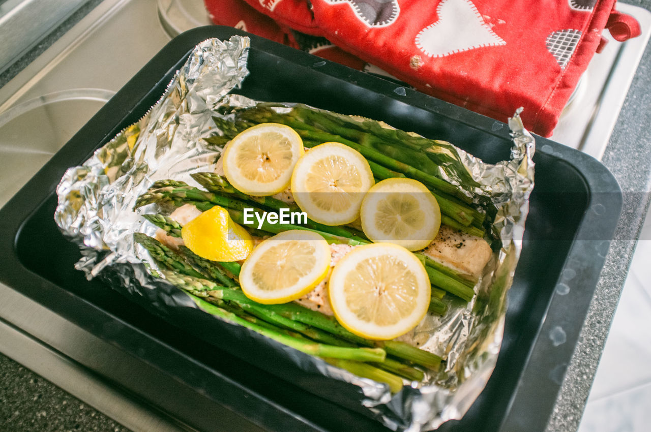 Lemon slices and asparagus with salmon on foil in container