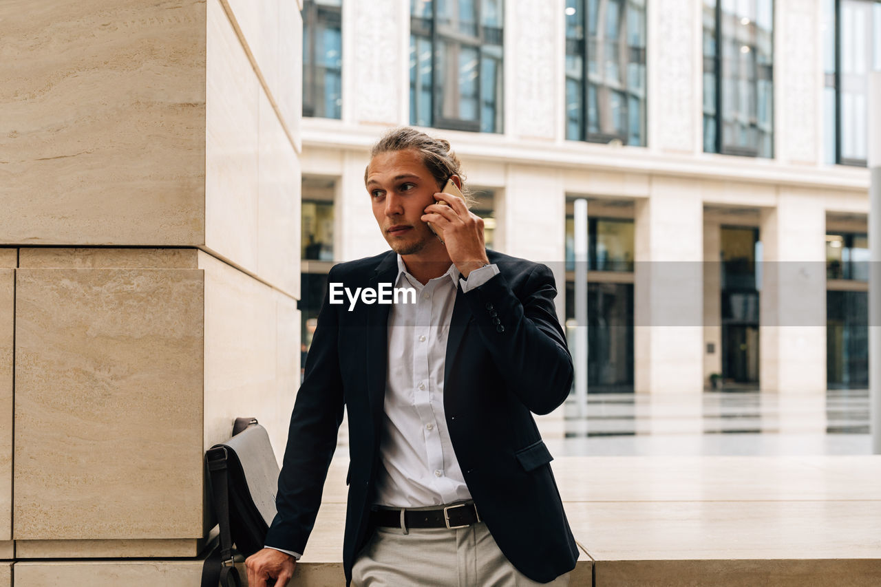 FULL LENGTH OF MAN USING PHONE WHILE STANDING AGAINST BUILDING