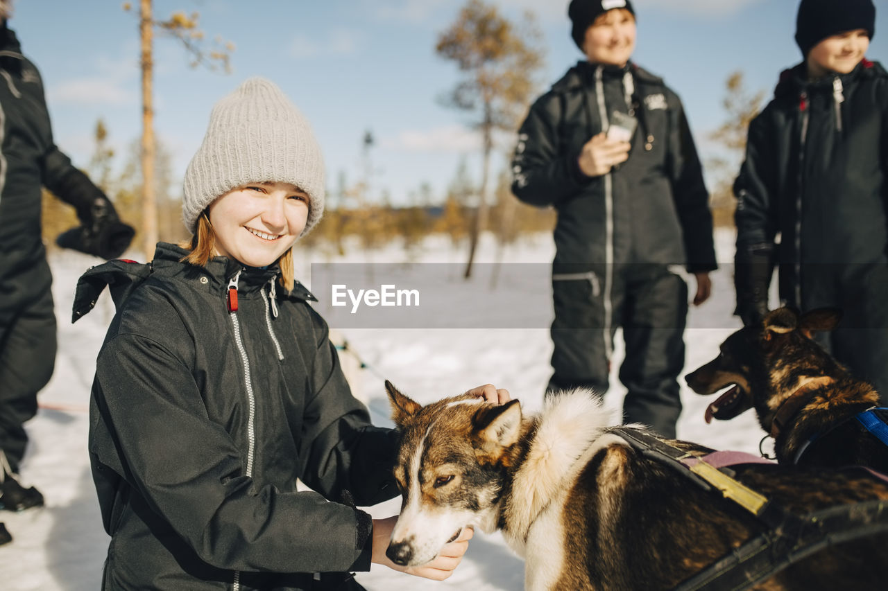 Portrait of smiling teenage girl stroking husky dog during winter