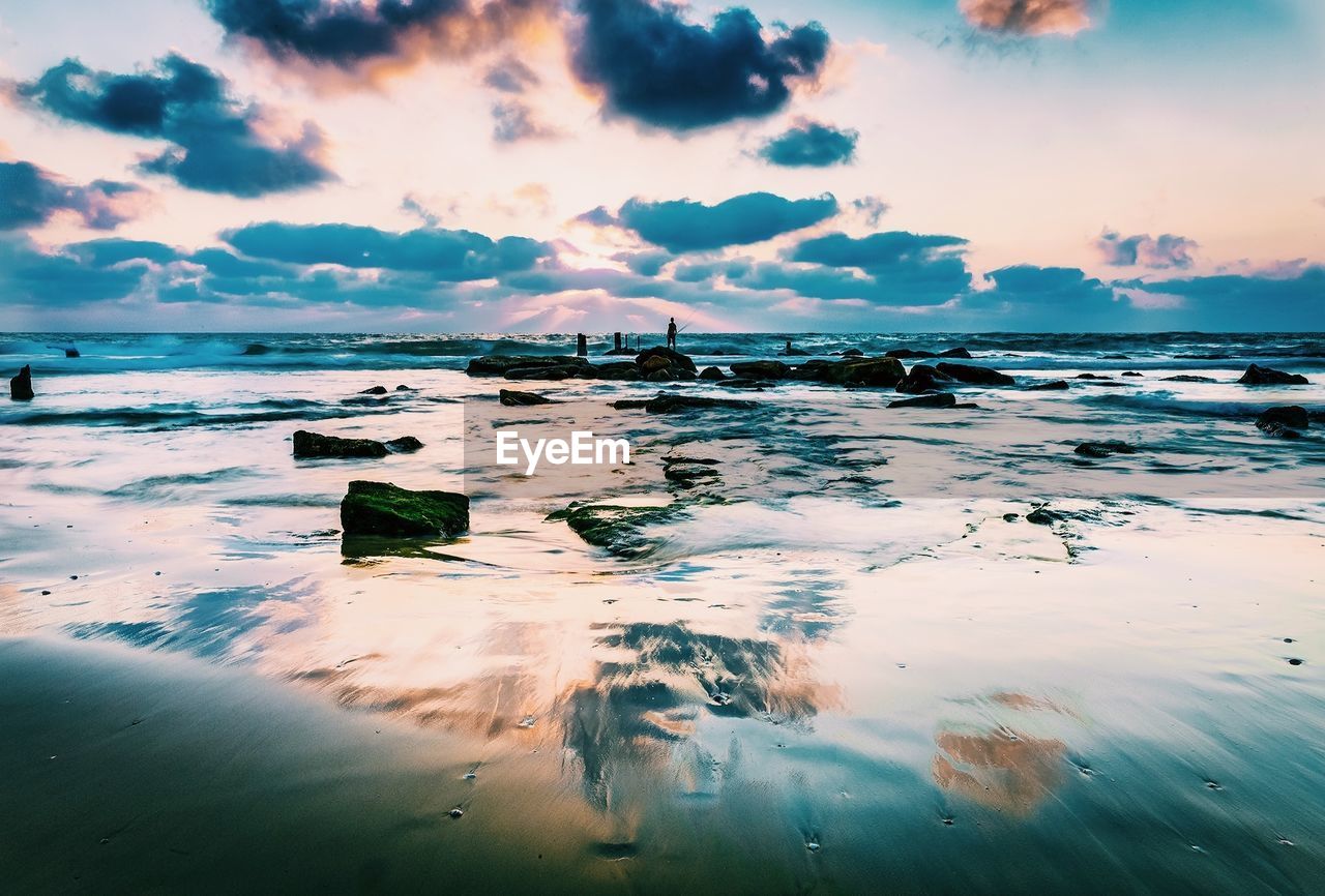 Scenic view of sea against cloudy sky during sunset