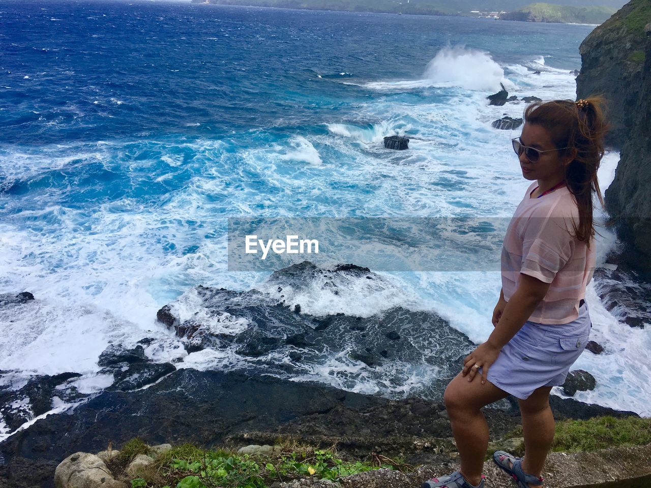 High angle view of woman standing on cliff against blue sea