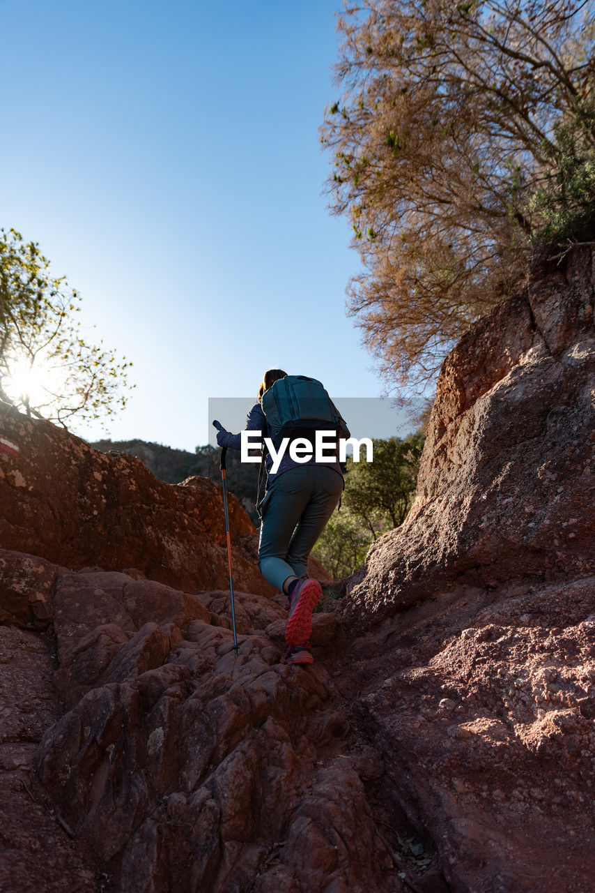 Woman climbs the mountain in the garraf natural park, supported by hiking sticks.