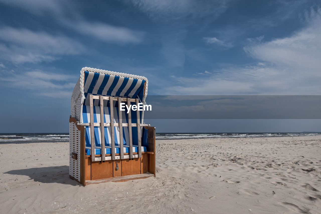 Hooded chair on beach against sky