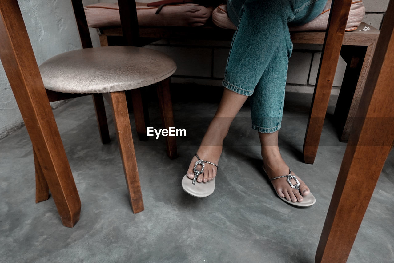 LOW SECTION OF WOMAN STANDING ON CHAIR IN ROOM