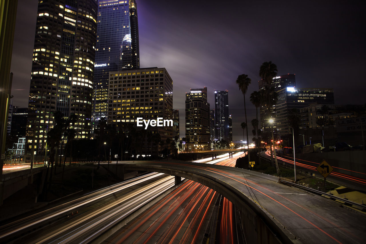 Light trails on road amidst illuminated buildings in city at night