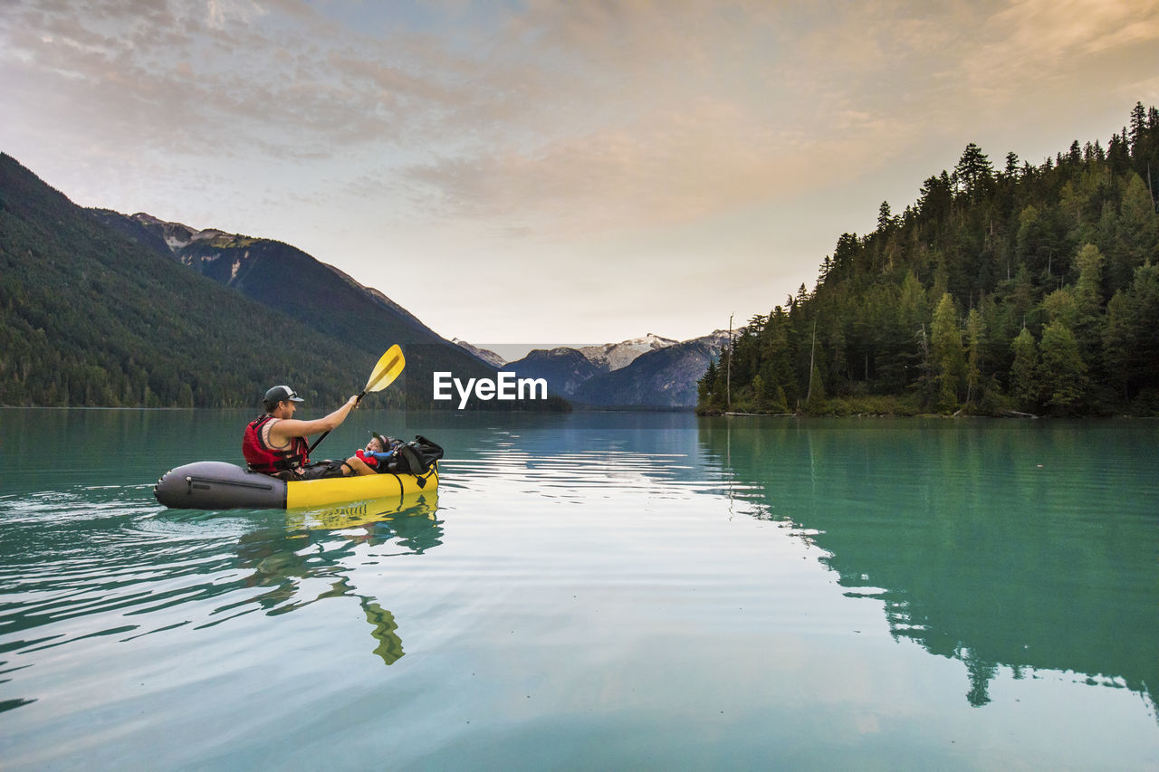 Father paddling inflatable boat with son on lake.