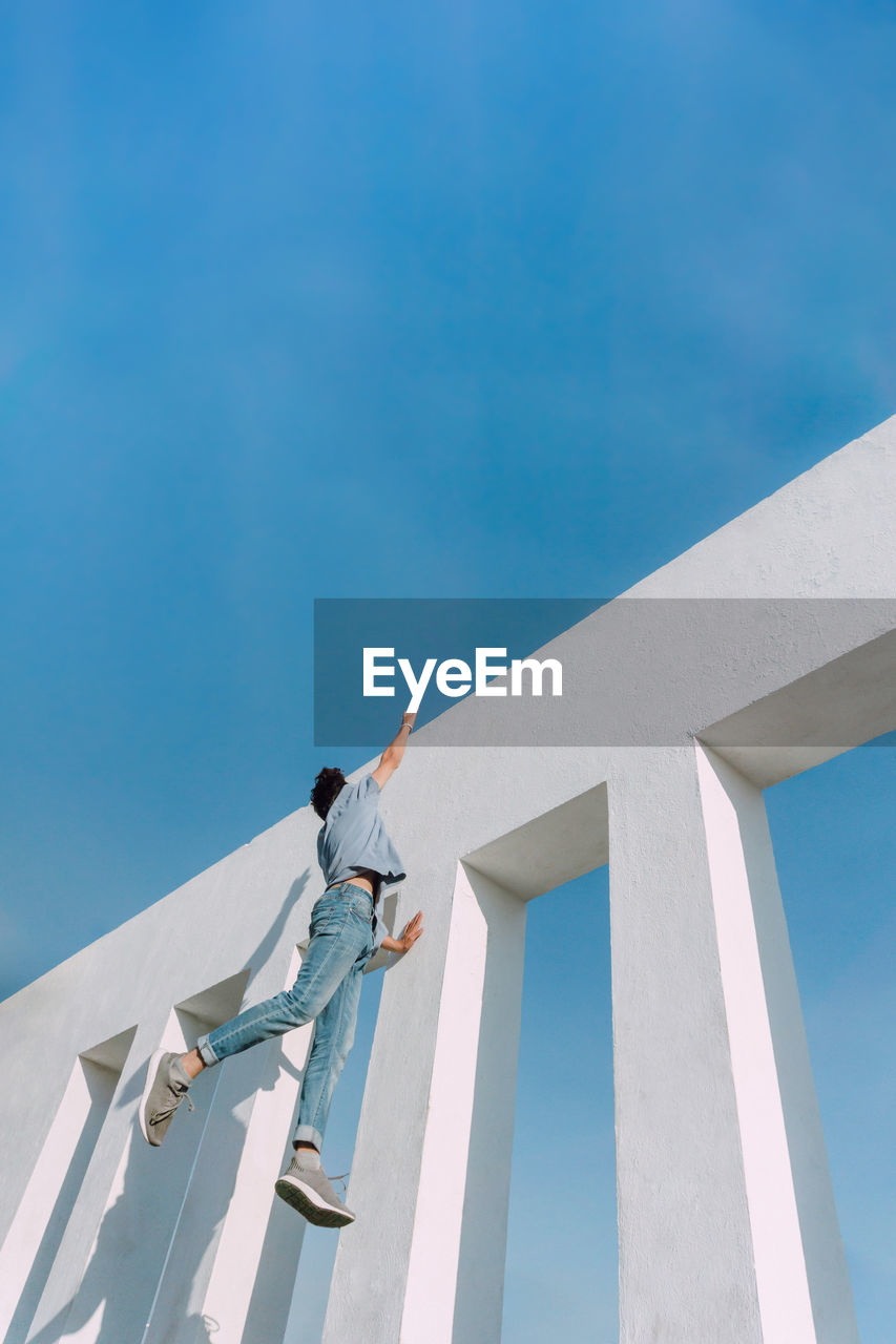 From below of anonymous fearless male hanging on edge of concrete wall and showing risky parkour trick