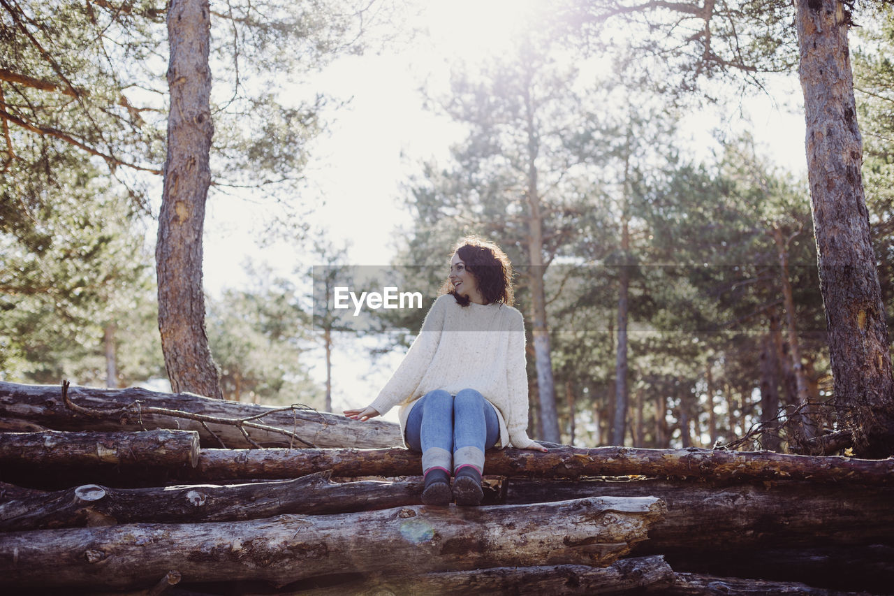 Full length of woman sitting on fallen trees in forest