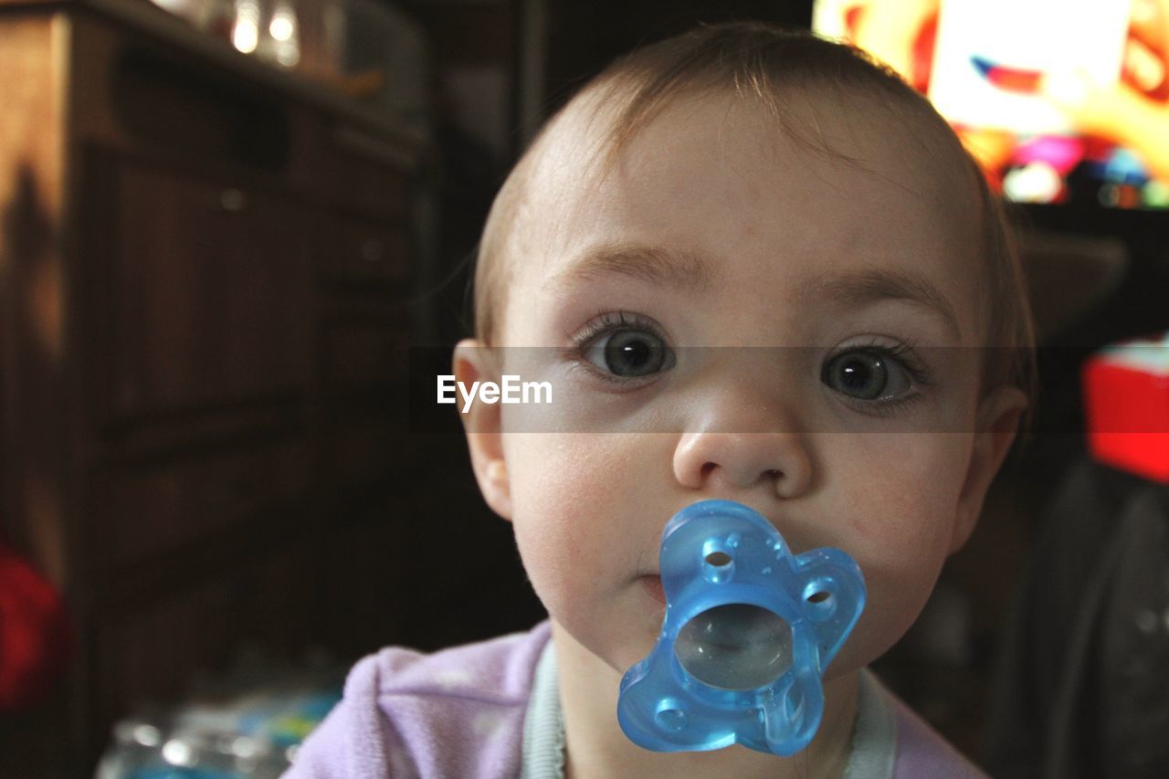 Close-up portrait of cute baby girl sulking pacifier at home