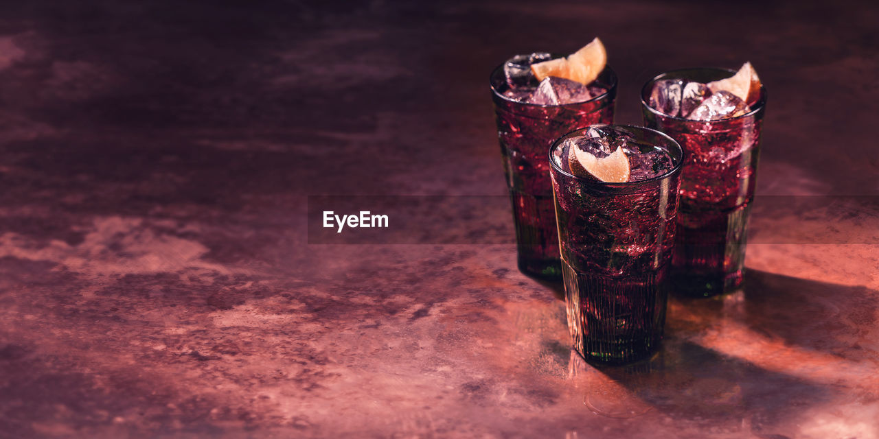 Alcoholic drink with lemon and ice, red lighting, marble table