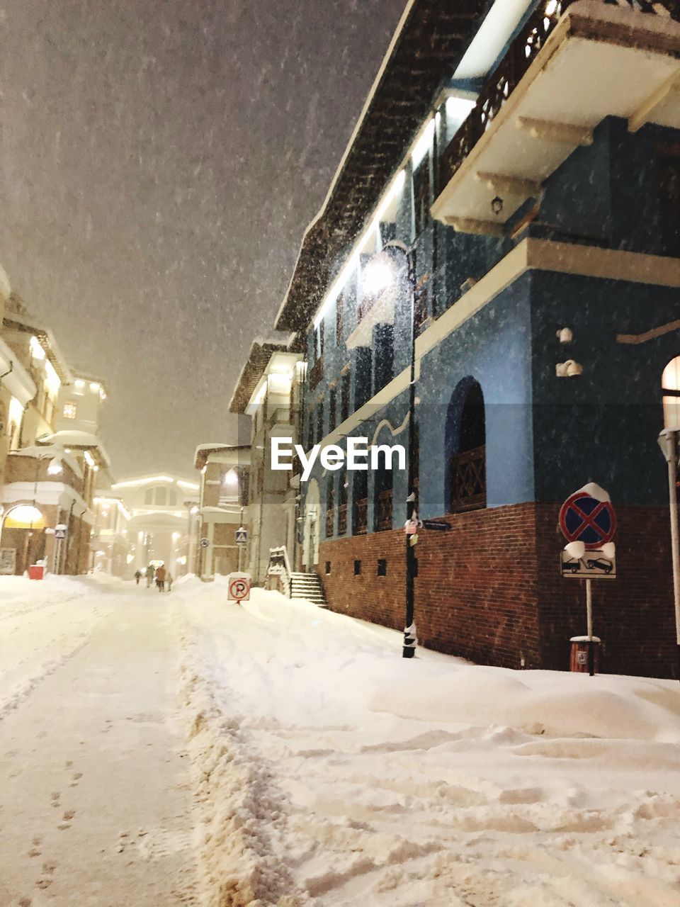 ROAD AMIDST SNOW COVERED BUILDINGS AT NIGHT