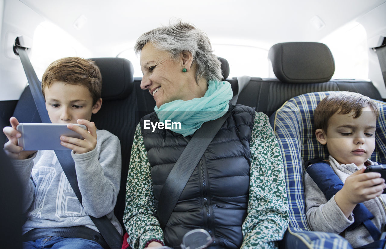 Senior woman looking at grandson using smart phone in car