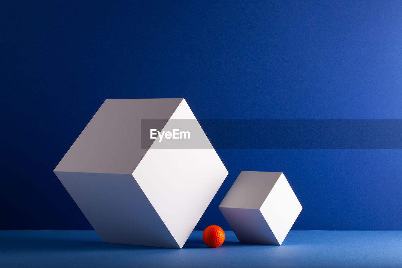 Two cubes with orange golf ball on the blue background