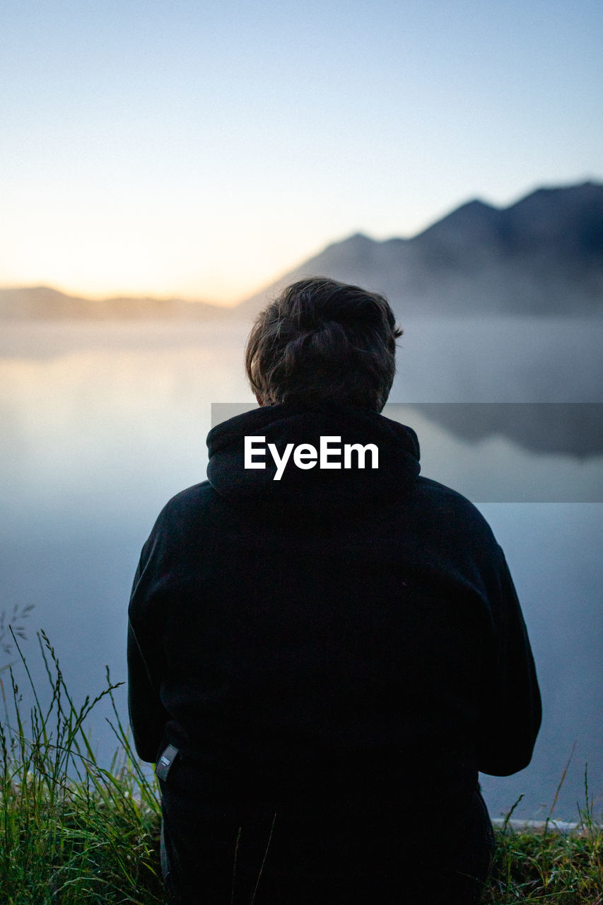 REAR VIEW OF MAN LOOKING AT MOUNTAIN LAKE