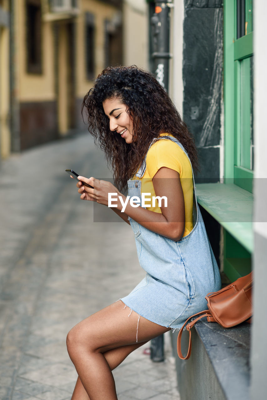 Side view of young woman using phone at alley