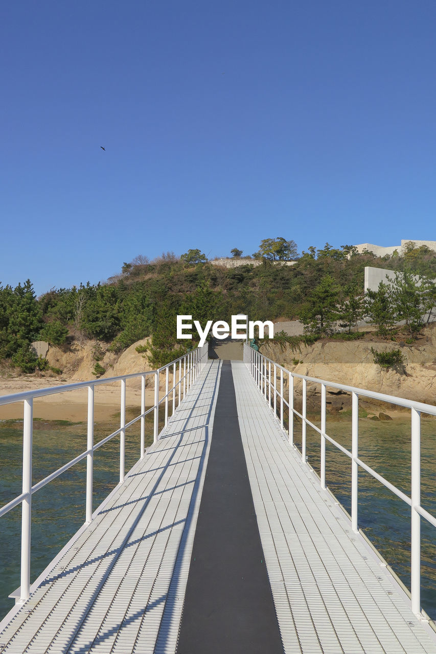 Footbridge on sea against clear blue sky