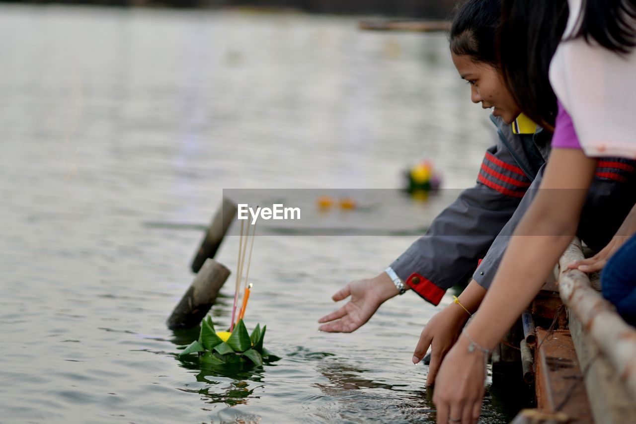 Side view of young woman putting incense with flower on lake