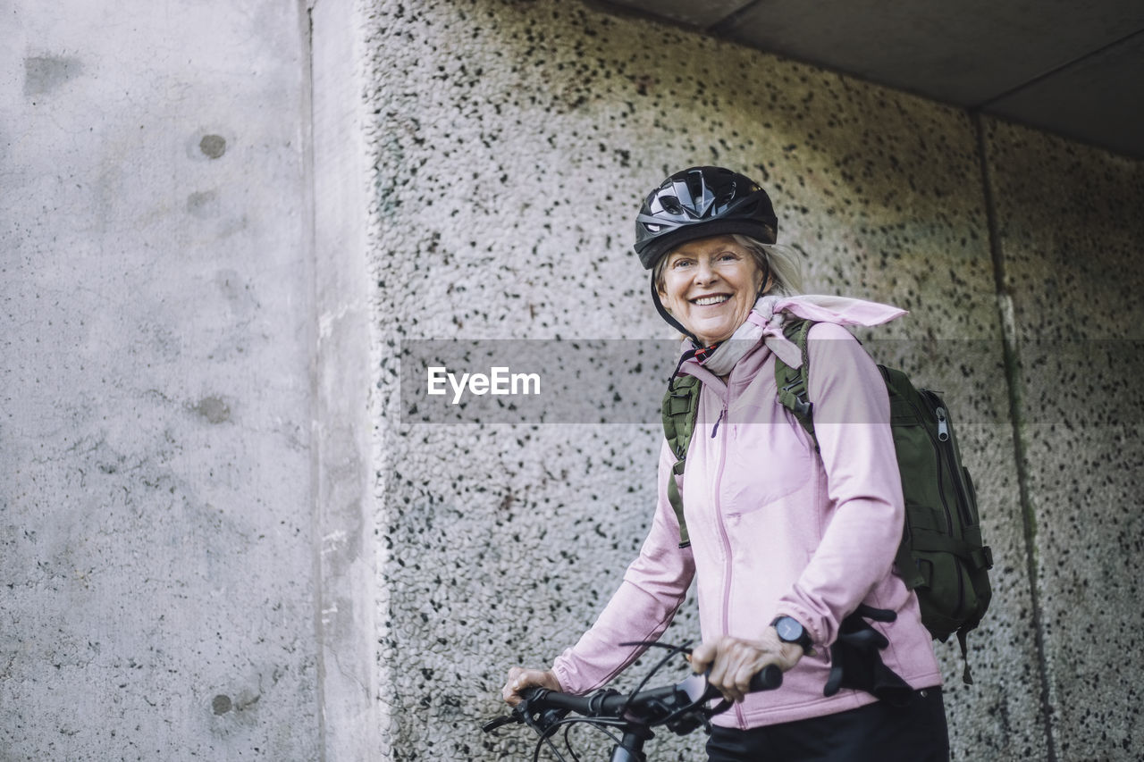 Portrait of senior woman with cycle standing near wall