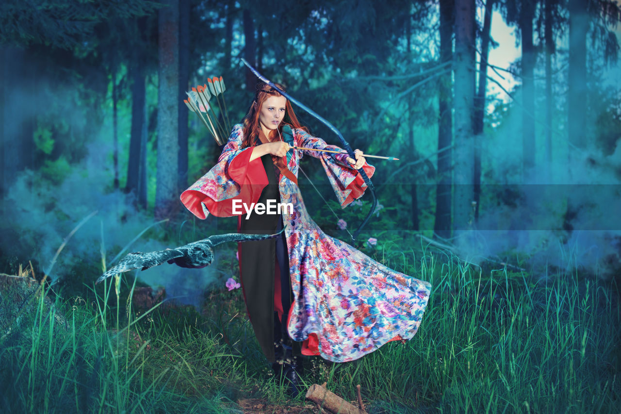 Young woman hunting with archery bow in forest 