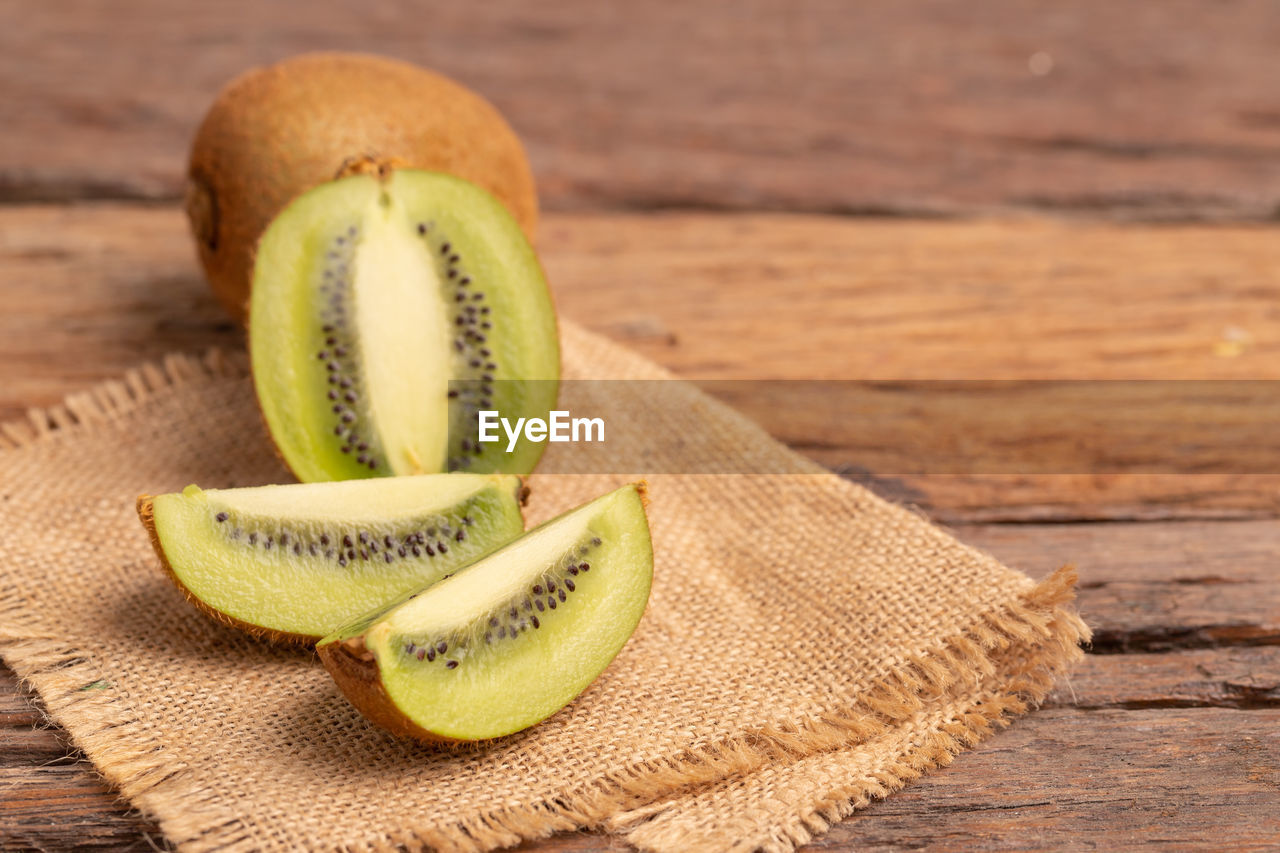 Slices of fresh kiwi on the brown sack placed on the old wooden table