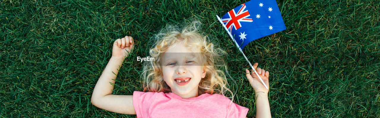 High angle portrait of cute girl holding australian flag lying on grass