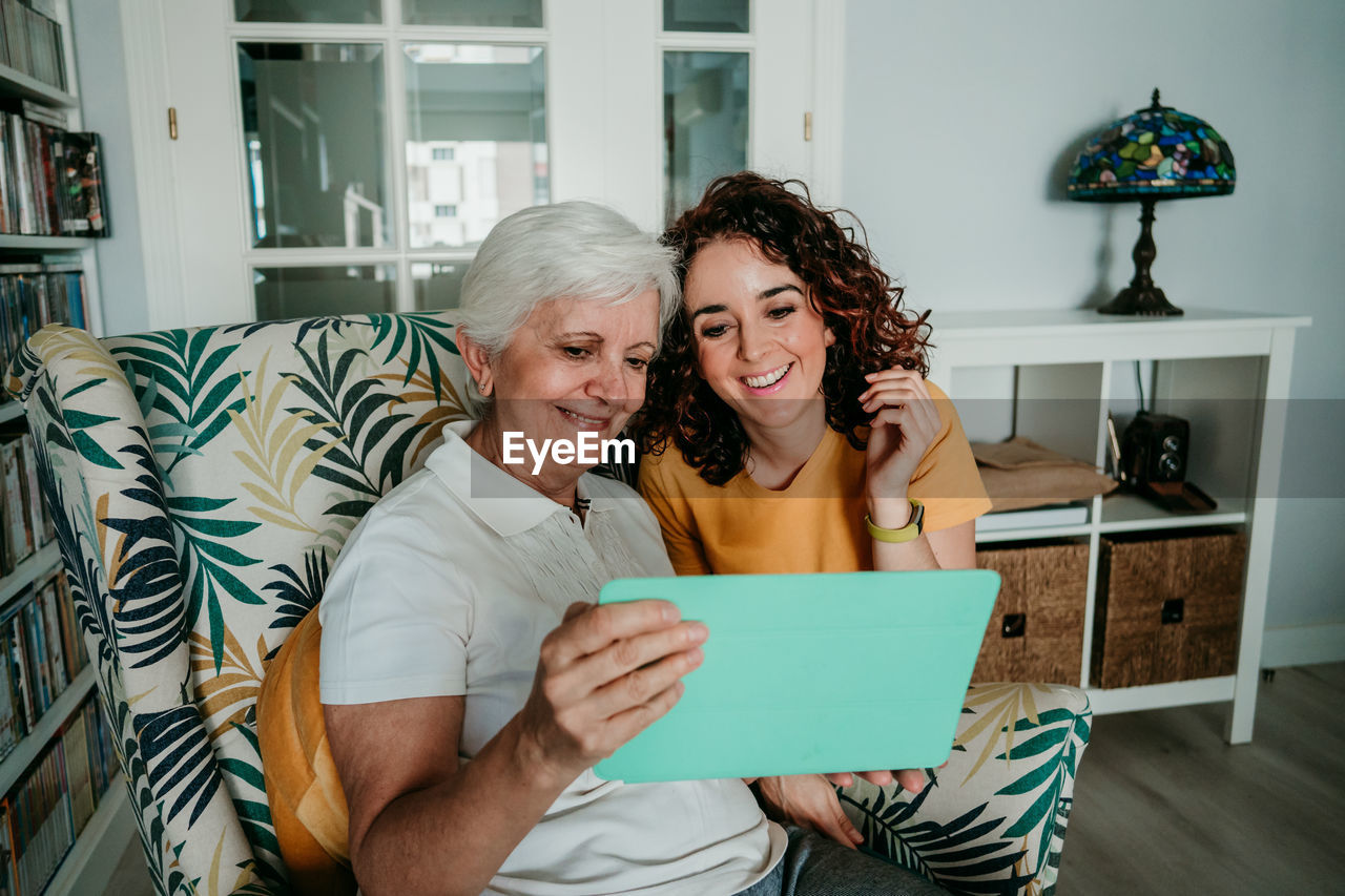 Smiling mother watching video with daughter over digital tablet at home