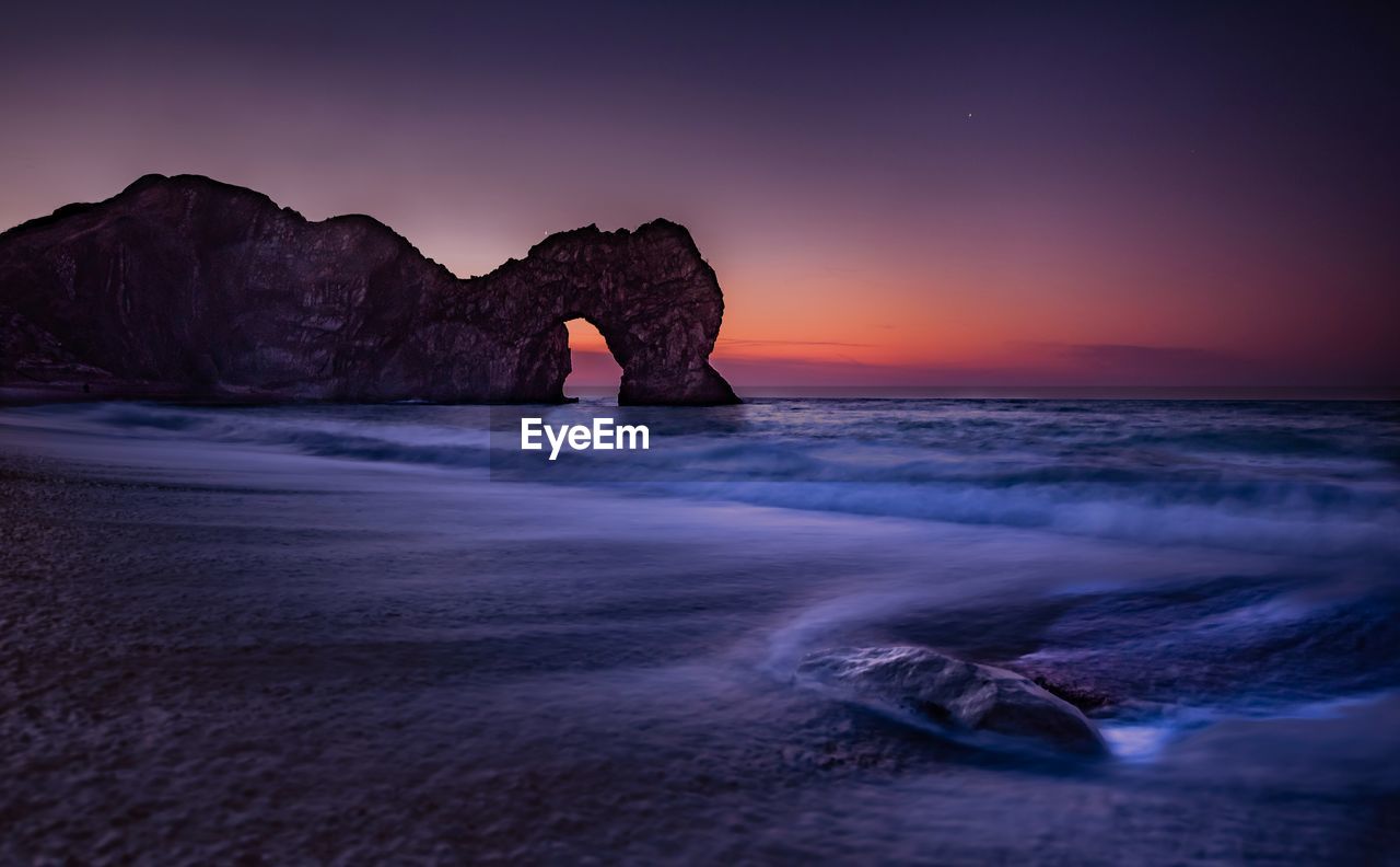 Scenic view of rocks in sea against sky during sunset